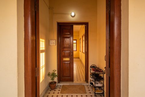 Indian apartment entrance passage in warm afternoon light, panelled teak door, mosaic tile floor, shoe rack